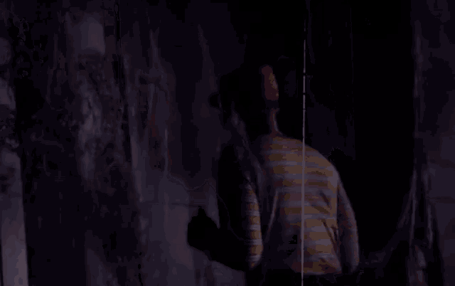a man in a striped shirt is standing in a dark room looking at a wall .