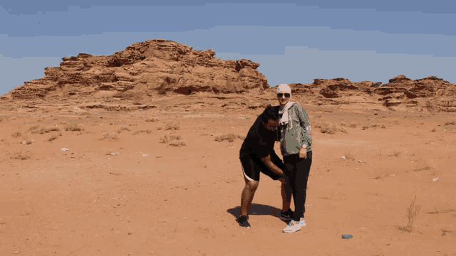 a man and a woman are standing in the desert and the man is wearing a green jacket with the letter j on it