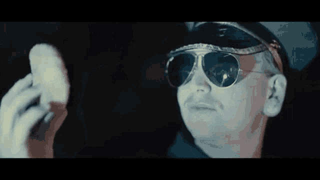 a man wearing sunglasses and a hat is holding a piece of bread in his hand .