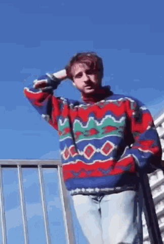 a man in a colorful sweater is standing on a railing