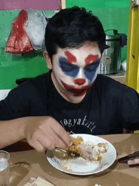 a man with a clown face painted on his face eating a plate of food