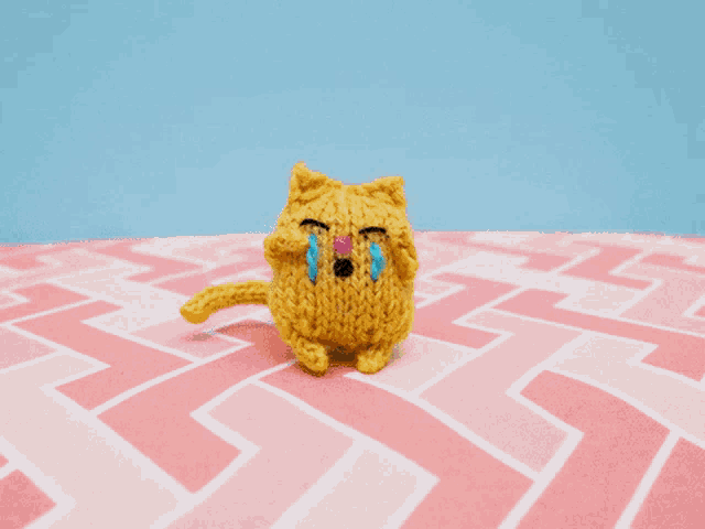 a knitted cat is crying on a pink and white patterned surface