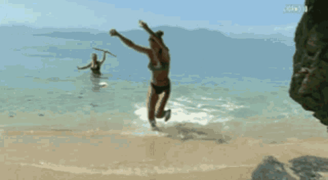 a woman in a bikini is dancing on the beach