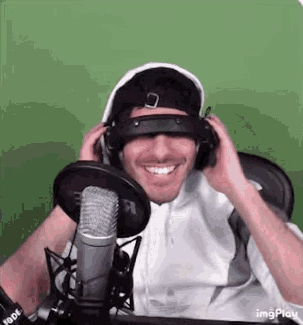 a man wearing headphones and sunglasses is smiling in front of a microphone .