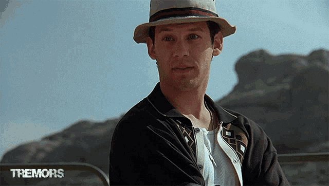 a man wearing a hat and a black jacket is standing in front of a sign that says tremors