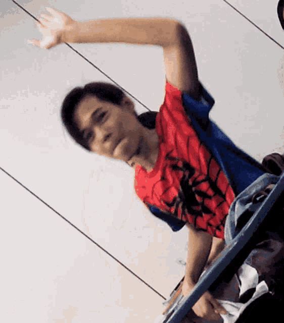 a man wearing a spiderman shirt is sitting on a chair with his arm outstretched