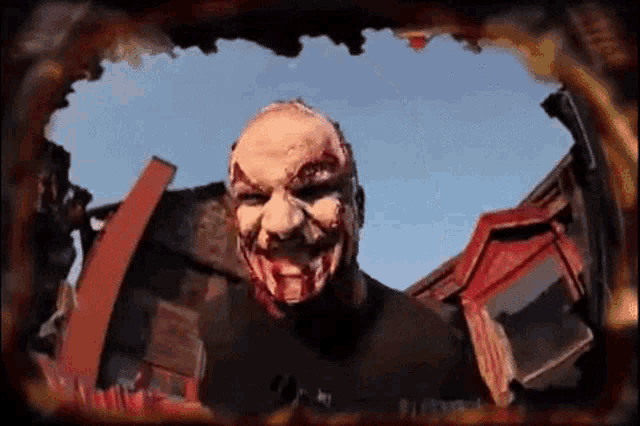 a clown with blood on his face is standing in front of a burning building