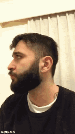 a man with a beard and a tattoo on his neck is standing in front of a white curtain .