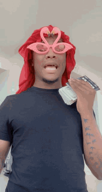 a man wearing flamingo glasses and a red head scarf holds a bunch of money