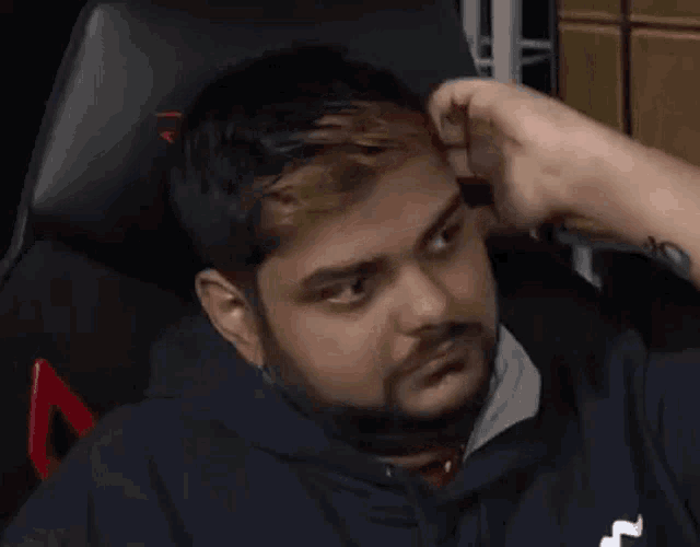 a man with a beard is sitting in a chair with his hand on his forehead and looking at the camera .