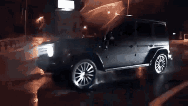 a jeep is driving down a wet street at night with its hood open .
