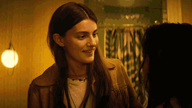 a woman in a brown jacket smiles while talking to another woman