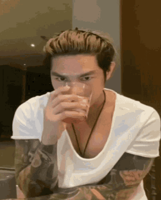 a man with tattoos on his arms is drinking a glass of red liquid