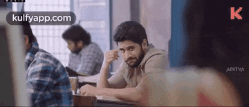 a man is sitting at a table in a restaurant with his hand on his face .