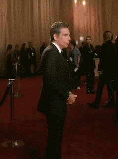 a man in a tuxedo and tie stands on a red carpet