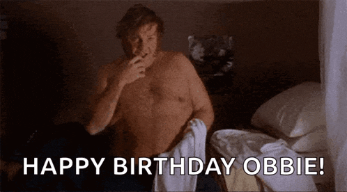 a shirtless man is sitting on a bed smoking a cigarette and says happy birthday obbie .