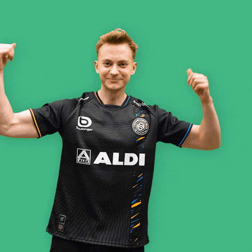 a man flexes his muscles in front of a green background wearing an aldi shirt