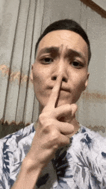 a man is holding his finger to his nose and making a funny face .