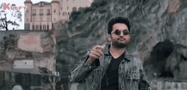 a man wearing sunglasses and a fringed jacket is standing in front of a building .