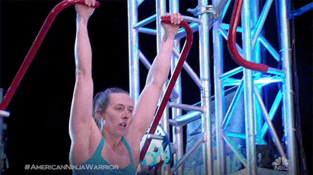 a woman in a blue tank top is hanging upside down on a nbc advertisement for american ninja warrior