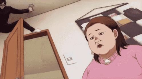 a woman in a pink sweater is standing in a room with a man sitting on the floor behind her .