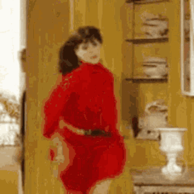 a woman in a red dress is dancing in a room with a yellow wall .