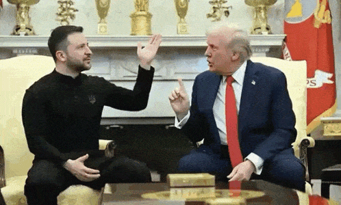 a man in a suit and tie is sitting next to a man in a black shirt and giving him a high five .