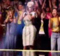 a woman in a white dress stands in front of a crowd applauding