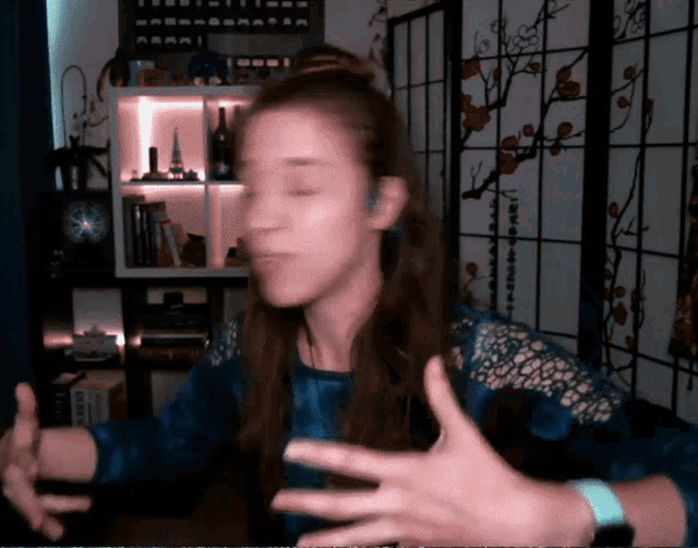 a woman in a blue shirt is making a face in front of a wall with a clock on it