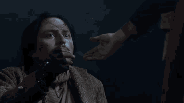 a man with a gun in his hand is being held by another man in a dark room