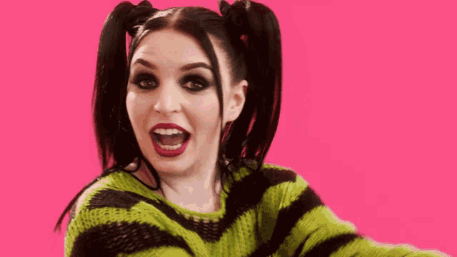 a woman with pigtails is singing into a green microphone on a pink background