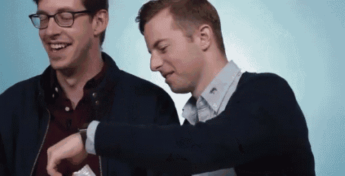 two men are looking at each other 's wristwatches and smiling .