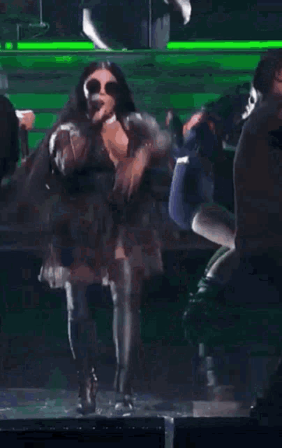 a woman is singing into a microphone while standing on a stage surrounded by people