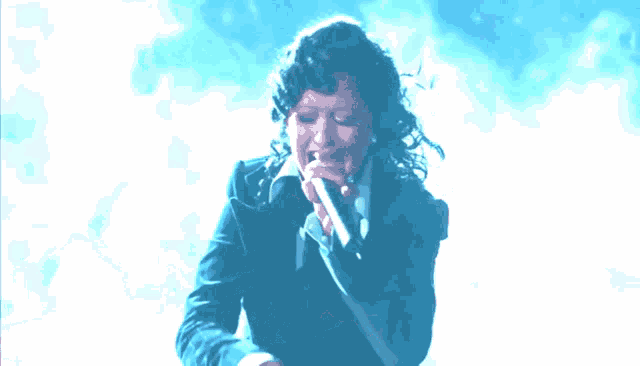 a woman is singing into a microphone with a blue background