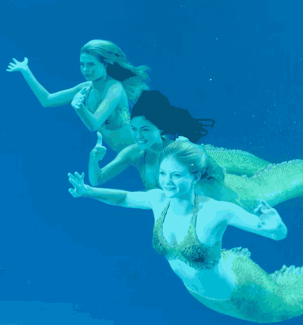 three mermaids are swimming in the water and one of them is giving a thumbs up