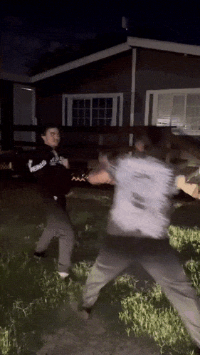 two men are fighting in front of a house with one wearing a hoodie that says reebok on it