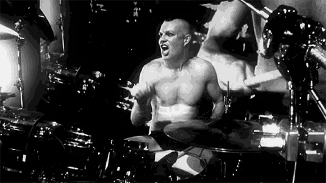 a shirtless bald man is playing drums in a black and white photo