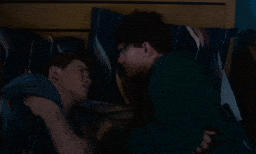 two young men are sleeping on a bed with blue pillows
