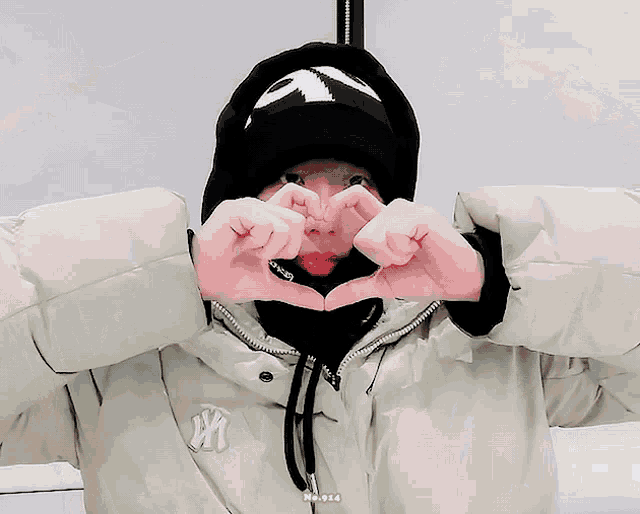 a person making a heart shape with their hands while wearing a ny jacket