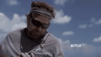 a man wearing sunglasses and a headband is standing in front of a netflix logo .