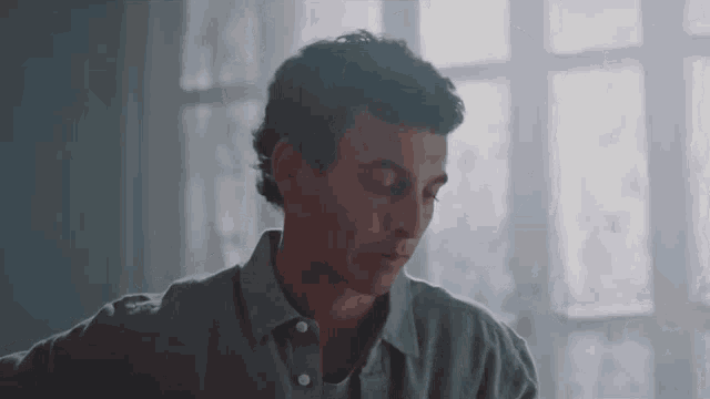 a man is sitting at a table in front of a window looking down .