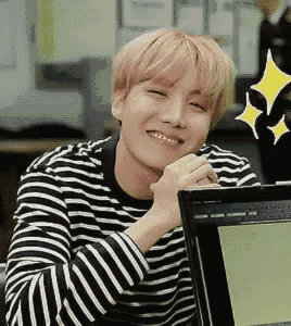 a young man wearing a striped shirt is smiling while sitting in front of a computer screen .
