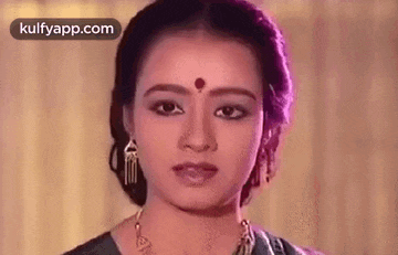 a close up of a woman 's face with a red dot on her forehead and earrings .