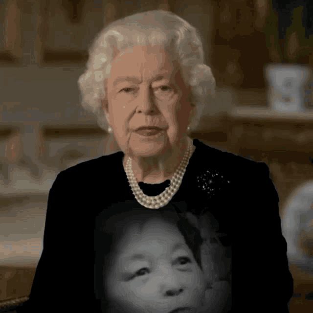 queen elizabeth wearing a pearl necklace and a black shirt with a picture of a child on it