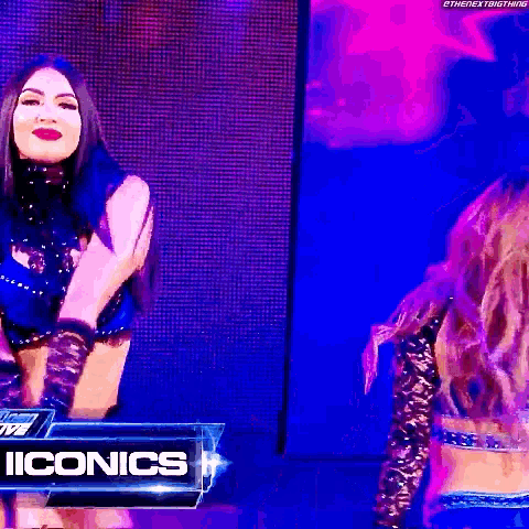 two women are standing on a stage in front of a sign that says iconics .