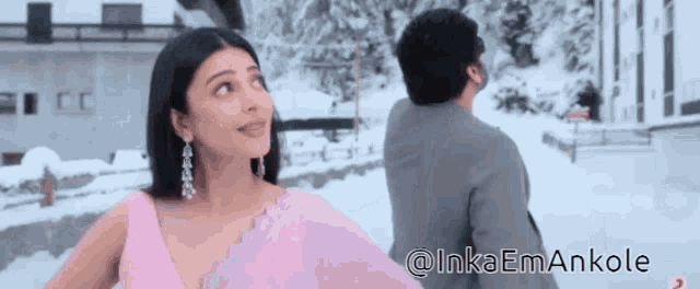 a woman in a pink dress is standing next to a man in a grey suit in the snow