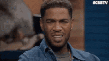 a man in a denim shirt is making a funny face while sitting on a stage .
