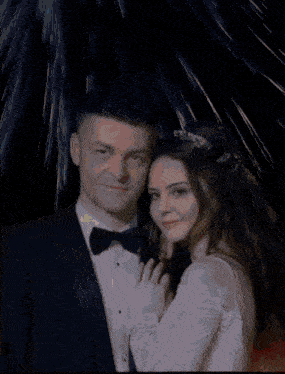 a bride and groom pose for a picture in front of fireworks
