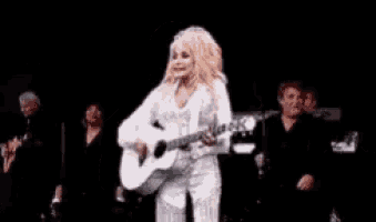 a woman in a white dress is playing a white guitar on stage .