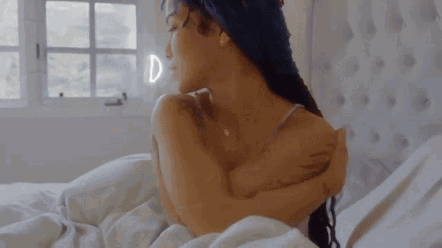 a woman is laying on a bed with her arms crossed and a window in the background .